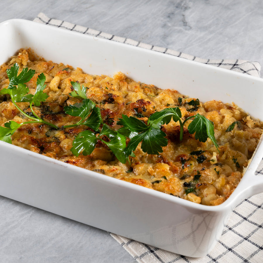 White rectangular baking dish of beans with breadcrumbs on a checkered cloth with a gray background