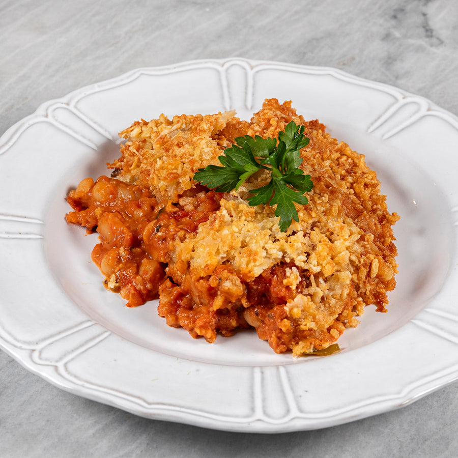 White plate with a serving of bean and tomato dish with breadcrumbs and parsley on a marble surface
